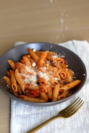 Sprinkling parmesan cheese on a plate of pasta with tomato sauce and eggplant. Selective focus.の写真素材
