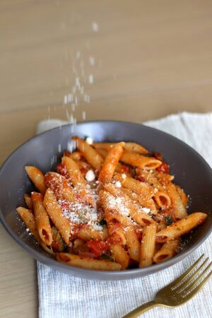 Sprinkling parmesan cheese on a plate of pasta with tomato sauce and eggplant. Selective focus.の写真素材