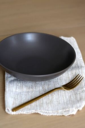 Empty brown plate with golden fork and beige napkin, set on a wooden table. Selective focus.の写真素材