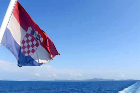 Flag of Croatia blowing in the wind. Croatian coast and islands in the background.の写真素材