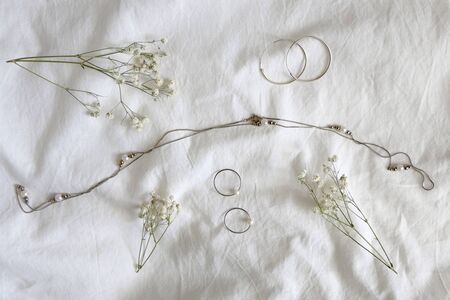 Silver and gold jewelry and gypsophila flowers on white sheets. Top view.の写真素材