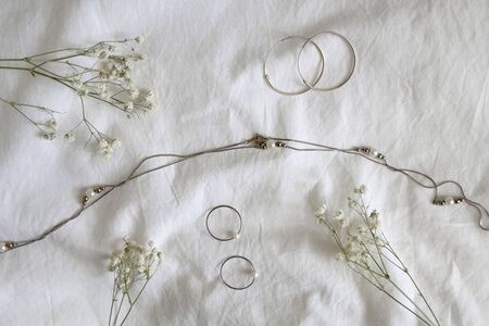 Silver and gold jewelry and gypsophila flowers on white sheets. Top view.の写真素材