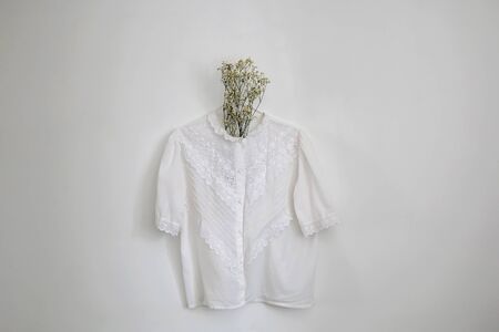 Vintage white lace blouse and gypsophila flowers, hanging on a white wall.の写真素材
