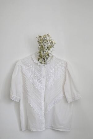 Vintage white lace blouse and gypsophila flowers, hanging on a white wall.の写真素材