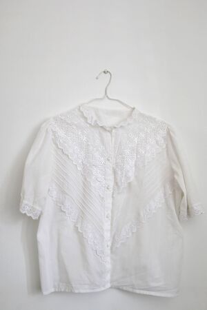 Vintage white lace blouse hanging on a white wall.の写真素材