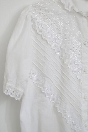 Vintage white lace blouse hanging on a white wall.の写真素材