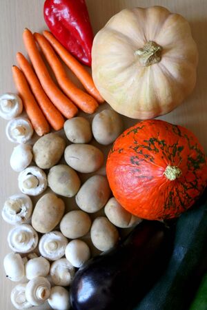 Pile of vegetables on a wooden table: pumpkin, squash, carrots, potatoes, eggplants, courgettes, peppers and mushrooms. Top view.の写真素材