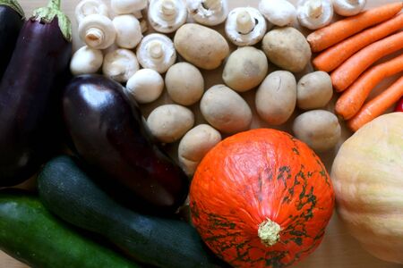 Pile of vegetables on a wooden table: pumpkin, squash, carrots, potatoes, eggplants, courgettes, peppers and mushrooms. Top view.の写真素材