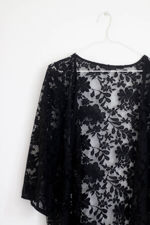 Black lace kimono top hanging in front of white wall.の写真素材