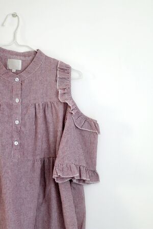 Pink blouse with ruffles and stripes, hanging on a white wall.の写真素材