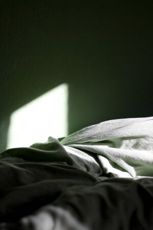 Green sheets on a bed and green wall, illuminated by sunlight. Selective focus.の写真素材