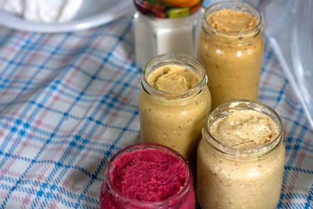 Jars filled with various homemade dips (hummus, beetroot, pate) on a picnic blanket. Selective focus.の写真素材