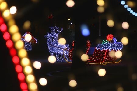 Outdoor Christmas decorations, shaped liked Santa's sleight, illuminated at night. Selective focus, defocused bokeh in the foreground.の写真素材