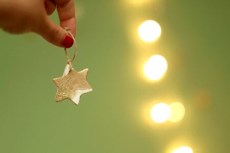 Hand holding star shaped Christmas ornament. Selective focus, green background.の写真素材