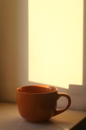 Cup of tea on a window sill, illuminated by warm sunset light. Selective focus.の写真素材