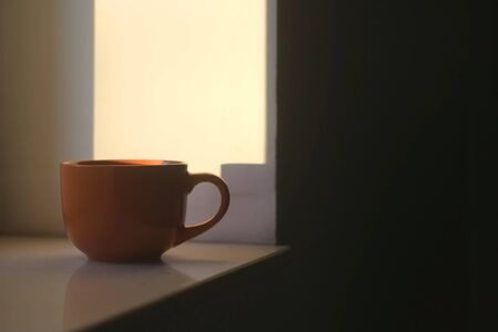 Cup of tea on a window sill, illuminated by warm sunset light. Selective focus.の写真素材
