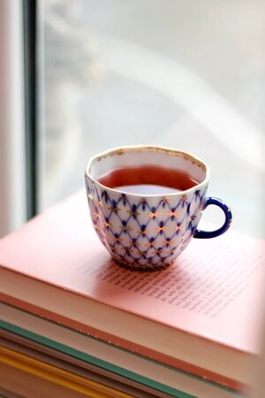 Tea in a vintage porcelain cup on stack of pastel colored books. Selective focus.の写真素材