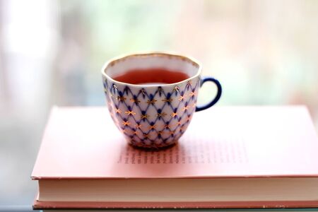Tea in a vintage porcelain cup on stack of pastel colored books. Selective focus.の写真素材