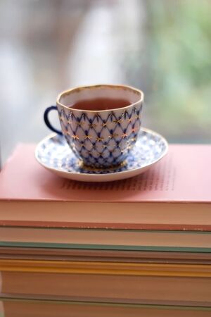 Tea in a vintage porcelain cup on stack of pastel colored books. Selective focus.の写真素材