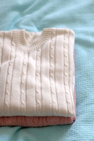 Pile of pastel and neutral colored sweaters on mint green background. Selective focus.