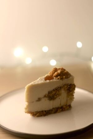 Slice of vegan cake with walnuts, cashew nuts and raisins. Selective focus, bokeh lights.の写真素材