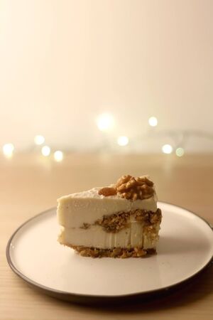 Slice of vegan cake with walnuts, cashew nuts and raisins. Selective focus, bokeh lights.の写真素材