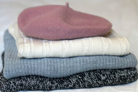 Stack of white, gray and black sweaters with pink beret. Selective focus.の写真素材
