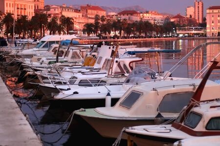 Small fishing boats and historic buildings on Riva promenade in Split, Croatia illuminated by pink sunset light. Selective focus.の写真素材