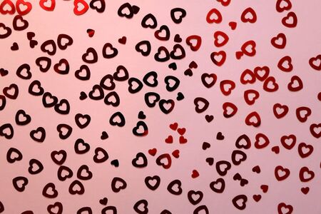 Red heart shaped confetti on pale pink background. Love and valentine concept. Top view.