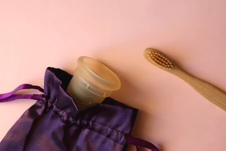 Menstrual cup and bamboo toothbrush on pastel pink background. Sustainable toiletries. Flat lay.の写真素材