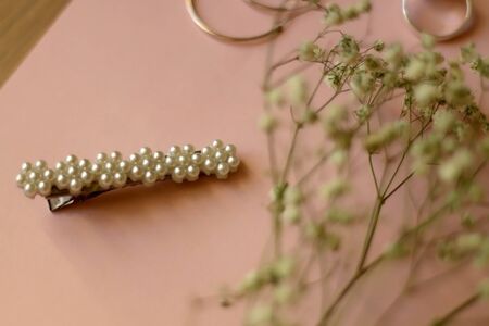 Fashionable accessories on pale pink background. Beret with pearls, silver gemstone ring and hoop earrings, with gypsophila flowers. Selective focus.の写真素材