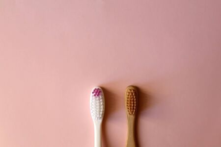 Plastic and bamboo toothbrush on pale pink background. Transition to zero waste lifestyle. Flat lay.