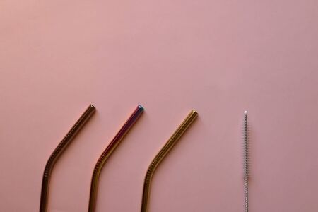 Reusable metal straws and cleaner, on pale pink background. Flat lay.