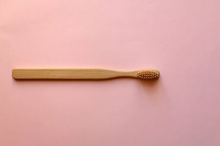Bamboo toothbrush on pale pink background. Zero waste lifestyle concept. Flat lay.