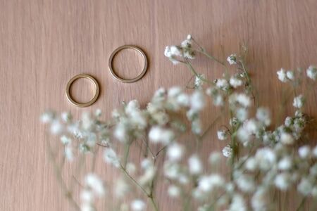 Two gold wedding rings and gypsophila flowers on wooden table. Selective focus.