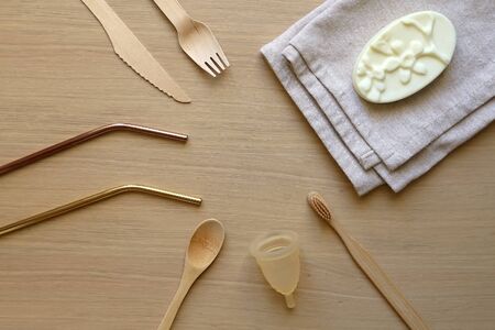 Various zero waste products on a wooden table: cloth, soap, cutlery, straws, toothbrush and menstrual cup. Top view.の写真素材