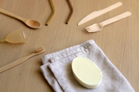 Various zero waste products on a wooden table: cloth, soap, cutlery, straws, toothbrush and...