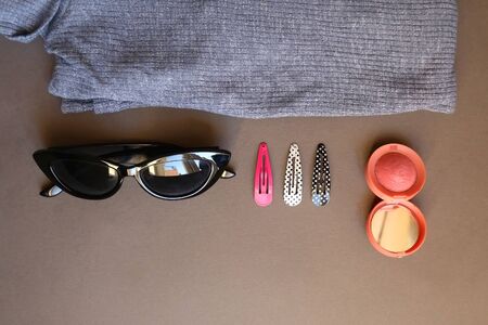 Blue turtleneck, pink blush, colorful hair clips and sunglasses on dark gray background. Top view.の写真素材