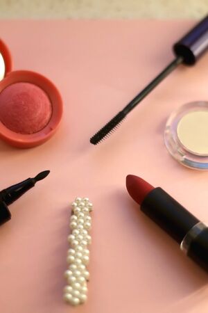 Make-up products on pale pink background: pink blush, mascara, highlighter, lipstick, eyeliner and fashionable beret. Selective focus.の写真素材