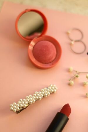 Beauty products and fashionable accessories on pale pink background: blush, mascara, eyeliner, lipstick,k rings, hoop earrings, beret and gypsophila flowers. Selective focus.の写真素材