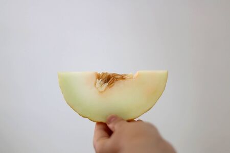 Unrecognizable person holding a slice of canary melon. Selective focus, white background.