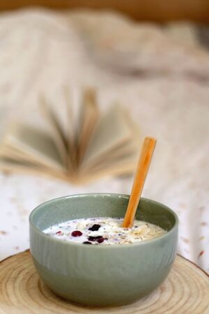 Breakfast bowl with milk, oats, chia seeds and berries, served on a bed with floral sheets. Open book in the background. Selective focus.の写真素材