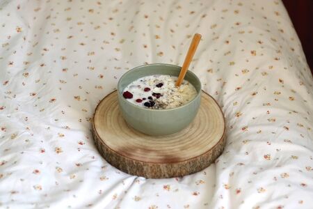 Breakfast bowl with oatmeal, berries, chia seeds and coconut chips on a bed with floral sheets. Selective focus.の写真素材