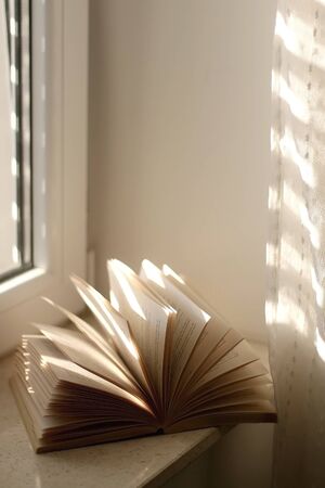Open book on a window sill, illuminated by sunlight. Selective focus.の写真素材