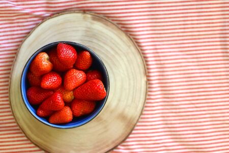 Bowl of fresh strawberries on a bed with striped bedding. Top view.の写真素材