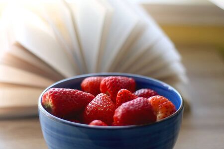 Bowl of fresh strawberries and open book on a table. Selective focus.の写真素材