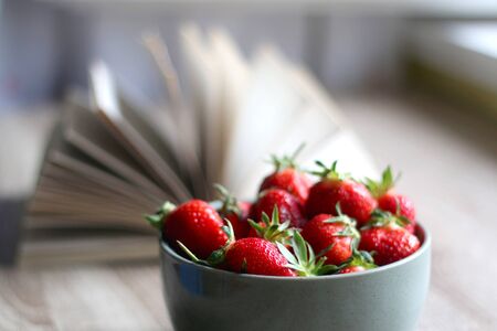 Bowl of fresh strawberries and open book on a table. Selective focus.の写真素材