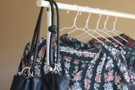 Black bag and black floral garments on a clothing rack. Selective focus.の写真素材