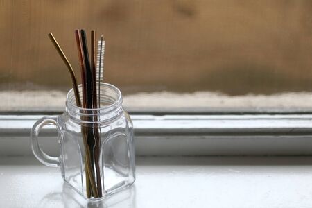 Reusable metal straws and cleaner in a glass jar. Selective focus.