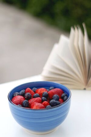 Bowl of strawberries and blueberries and open book in a garden. Selective focus.の写真素材